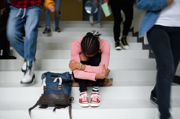 Depressed young student wearing face mask, studying alone on college stairs, head in hands