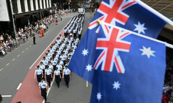 Rows of soldiers march down the street below two Australian flags