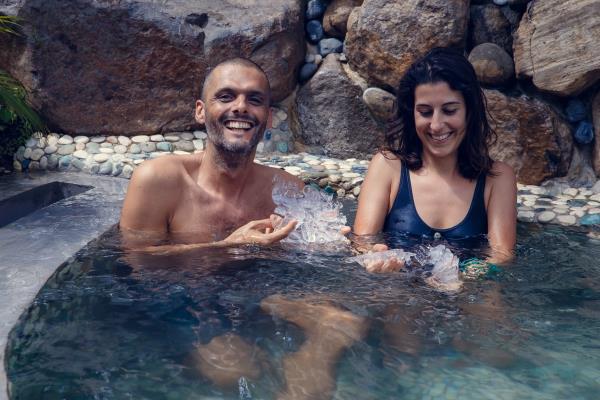 Young man and woman havin<em></em>g recreatio<em></em>nal bath in the water filled with ice cubes. Multiethnic couple getting cryo therapy outdoors