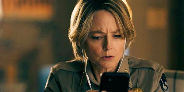 Jodie Foster looking at a phone with earbuds in in True Detective Night Country