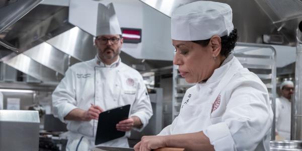 Liza co<em></em>lon-Zayas as Tina cooks as a teacher watches in The Bear season 2 episode 5